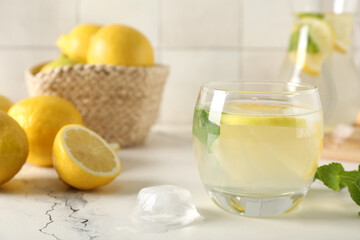 Glass of fresh lemonade with mint and lemons on white table, closeup