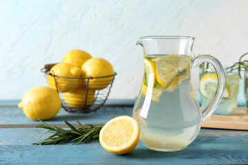 Jug of fresh lemonade with rosemary and lemons on blue wooden table