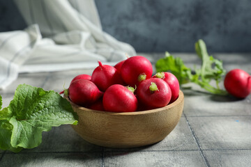 Wooden bowl with fresh radishes on grey tile table