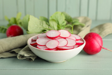 Bowl with slices of fresh radishes on green wooden background