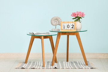 Wooden calendar with date 2 October, vase of beautiful flowers and magazines on coffee table near blue wall in living room