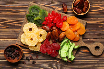 Cutting board and bowls with different candied fruits on wooden background