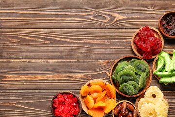 Bowls with different candied fruits on wooden background