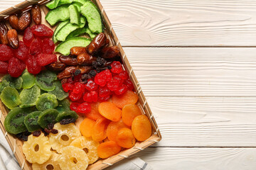 Wicker tray with different candied fruits on white wooden background