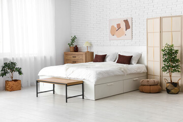 Interior of light room with big bed, folding screen and plants
