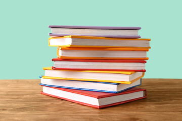 Stack of colorful books on wooden table against turquoise background