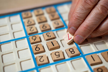 closeup hands carefully placing number into Sudoku puzzle, senior man focused on solving puzzle on wooden board, Brain exercise, cognitive health, and mental agility in mature age, brain health
