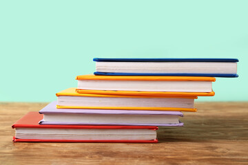 Stack of colorful books on wooden table against turquoise background