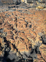 CLOSE UP: Fascinating textures of dried lava, stretching across a volcanic landscape under a clear sky. Warm brown and grey tones create a striking abstract visual of ancient geological formations.