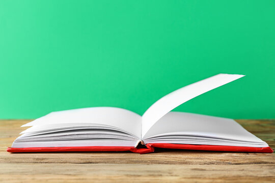 Open book on wooden table against green background