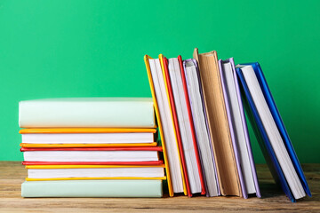 Many colorful books on wooden table against green background
