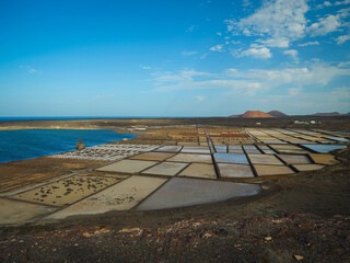 Rows of salt fields and evaporation ponds of Salinas de Janubio framed by volcanic coast and Atlantic Ocean. A picturesque view of the salt pans with traditional sea salt production in Lanzarote.