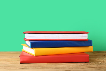 Stack of colorful books on wooden table against green background