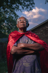 Elderly African American man wearing red cape, looking proudly upward in heroic stance, backyard at dusk. Great for concepts of inner strength, fantasy, senior empowerment, inspiration