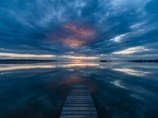 Obraz premium Serene sunset over calm lake with wooden dock