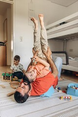 Father playing with his children on the floor in playroom.One child is held upside...
