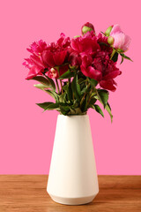 Vase with beautiful peony flowers on wooden table against pink background