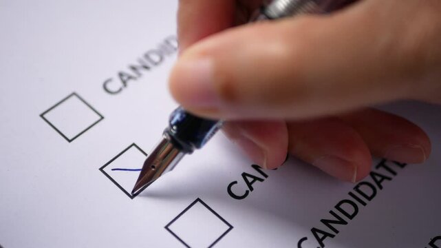 a person's hand holding a pen for marking a x cross on ballots to vote for a candidate. candidate election concept