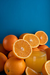 photo Freshly Squeezed Orange Juice Surrounded by Vibrant Whole and Halved Oranges Displayed Against a Deep Blue Background Highlighting Natural Citrus Fruit Appeal