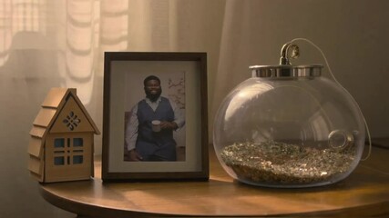 Still life featuring a framed photo, wooden house, and decorative glass jar