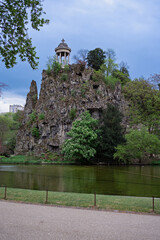 Temple de la Sibylle on a rocky cliff in Buttes-Chaumont Park, Paris. Scenic view with trees, lake, and dramatic sky. Iconic romantic landscape in spring