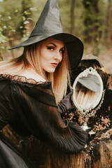 girl in a fluffy black dress and hat, halloween in the forest, magic with a mirror