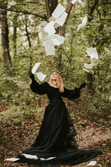 girl in a lush black dress and hat, halloween in the forest, magic with flying paper