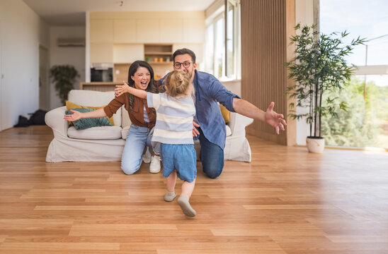 Happy young family with child enjoying new home after moving in – unpacking boxes, relaxing in living room, spending time together in kitchen, celebrating new beginning. Man, woman and daughter.