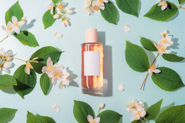 Perfume bottle placed among jasmine flowers and green leaves on a pastel blue surface. A gentle floral setup suitable for fragrance promotion and cosmetic branding. Top view, flat lay, mockup