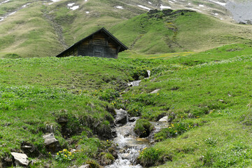 Idyllic Mountain Landscape with Green Meadow, Stream, and Rustic Cabin in Switzerland