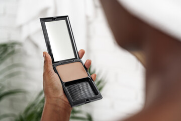 Person applying cosmetic powder in bathroom during morning routine with plants in the background