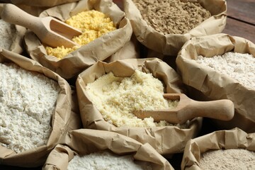 Different types of flour in paper bags on wooden table, closeup
