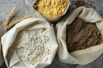 Different types of flour in bags on grey textured table, flat lay