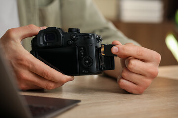 Man inserting SD memory card into photo camera at wooden table indoors, closeup