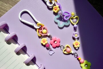 Cute girly colorful flower bag charm diy craft beads keychain object isolated on horizontal purple note book background.