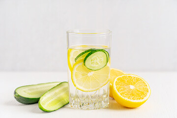 Refreshing healthy homemade detox water infused with juicy fresh slices of cucumber vegetable plant and cut lemon citrus fruit served in glass on white wooden table as summer cold antioxidant drink