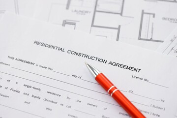 Pen on residential construction agreement and planning blueprints of residential building project