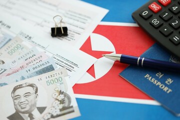 North Korean won money bills lies on table with pen, calculator, passport and tax forms