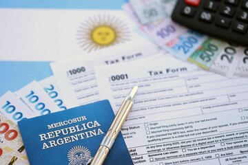 Argentine pesos money bills in big amount lies on table with pen, calculator, passport and tax forms