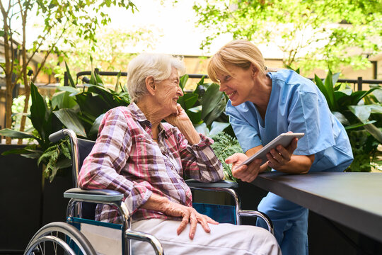 Nurse assisting senior in wheelchair with a digital device outdoors