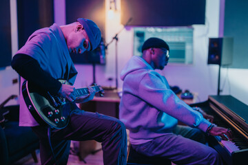 Two musicians collaborate in a music studio, playing guitar and piano, surrounded by a creative...