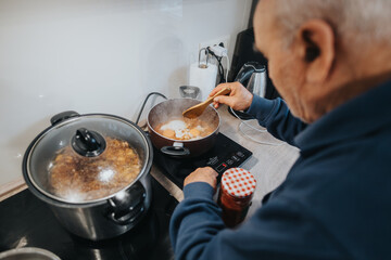 A senior individual is seen cooking on a modern stove, stirring ingredients in a saucepan to...