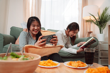 Asian Woman Friend Doing Lifestyle Indoor Smiling Phone Happiness, Sharing Joy and Memories Together at Home, Relaxing on Sofa with Smart Devices and Family Bonding Moments