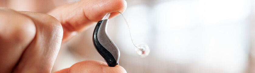 Macro shot of a senior woman's fingers holding a modern Philips hearing aid, highlighting assistive...