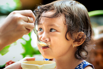 Mother's hand feeding healthy meal to a female Southeast Asian toddler with cute expression on her face