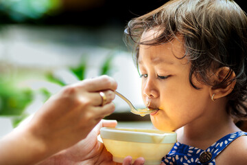 Mother's hand feeding healthy meal to a female Southeast Asian toddler with cute expression on her face