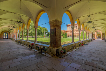 Ferrara, Italy - May 17, 2025: Monumental cemetery of the Charterhouse of Ferrara in Italy features a curved portico with arches and columns surrounding a green lawn under a clear blue summer sky