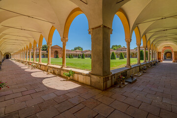 Ferrara, Italy - May 17, 2025: Wide angle view of the Charterhouse of Ferrara's cloister, featuring columns, arches, a green lawn, and a blue sky