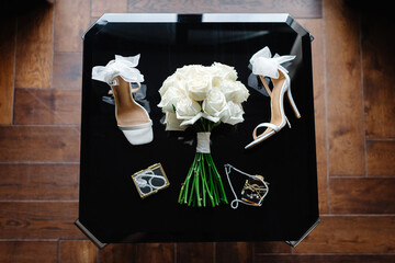 Elegant bridal accessories showcasing white roses bouquet, stylish heels, perfume, and jewelry on a...