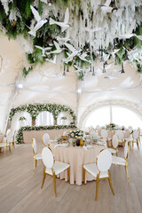 Elegant wedding reception hall featuring round tables, white and gold chairs, and floral arrangements